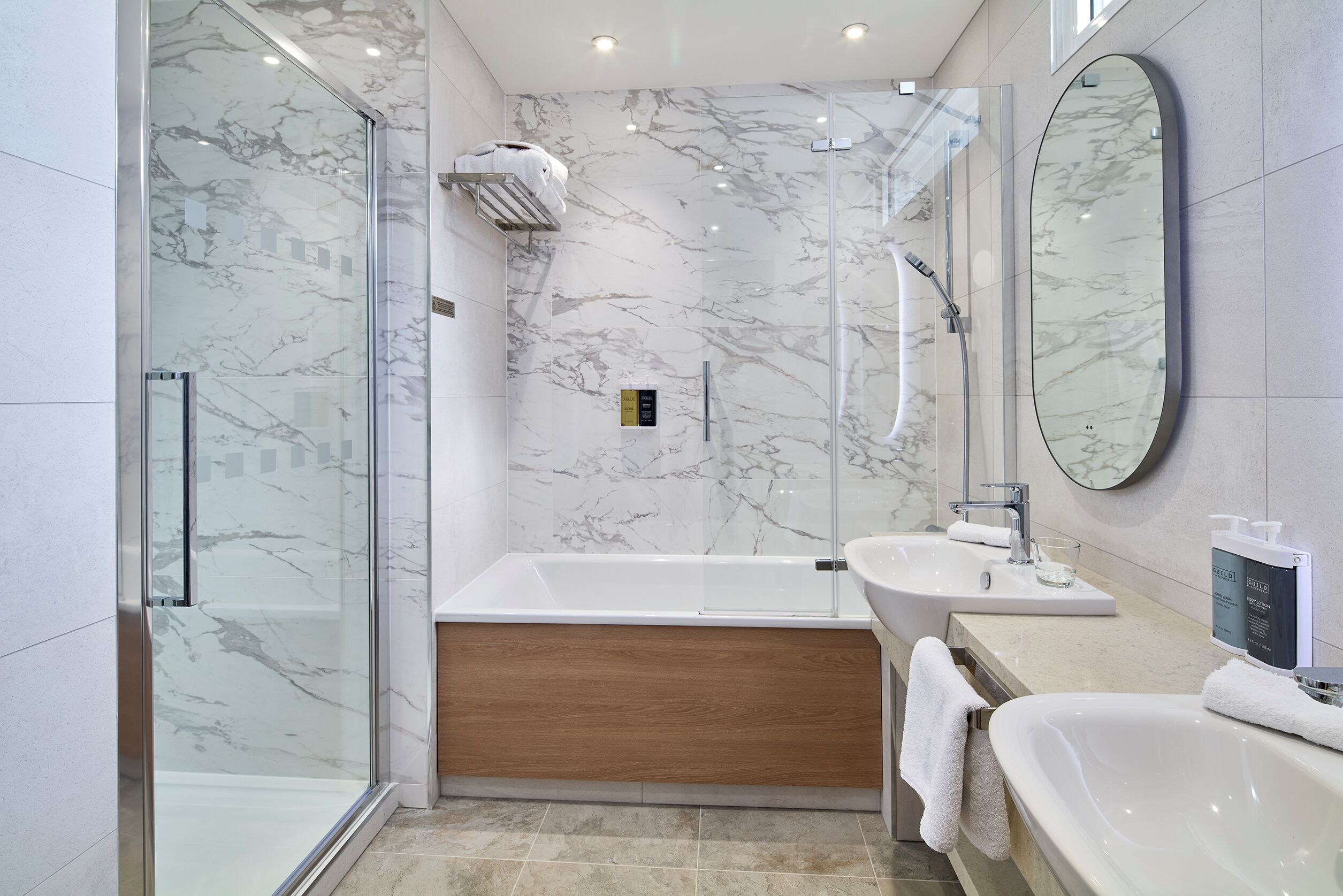 A modern bathroom with a glass-enclosed shower, a wooden bathtub, and two sinks.