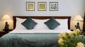 A neatly made bed with a green blanket and two pillows, flanked by two bedside lamps and framed artwork on the wall.