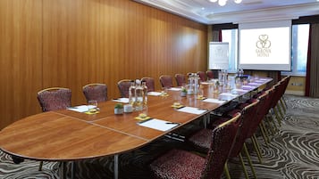 Un salón de conferencias con una larga mesa, sillas rojas con estampado y una pantalla proyectora mostrando el logotipo de Sarova Hotels.