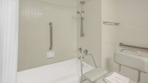 A bathroom with a bathtub, a shower, and a handrail.