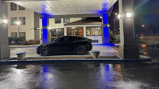 A black car parked at a hotel entrance with a covered driveway and blue lighting.