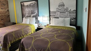 A hotel room with two beds, a brick wall, and two large black and white photographs on the wall.