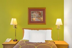 A hotel room with a bed, two bedside lamps, a nightstand with a phone, and a framed painting on the wall.