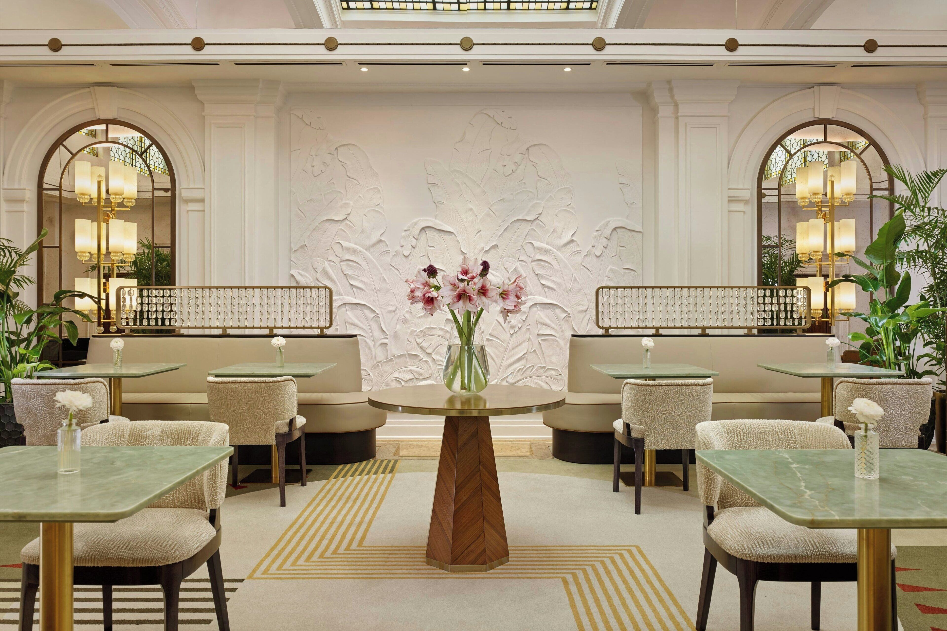 Un vestíbulo de hotel con mesas redondas, asientos acolchados y una pared decorativa central.