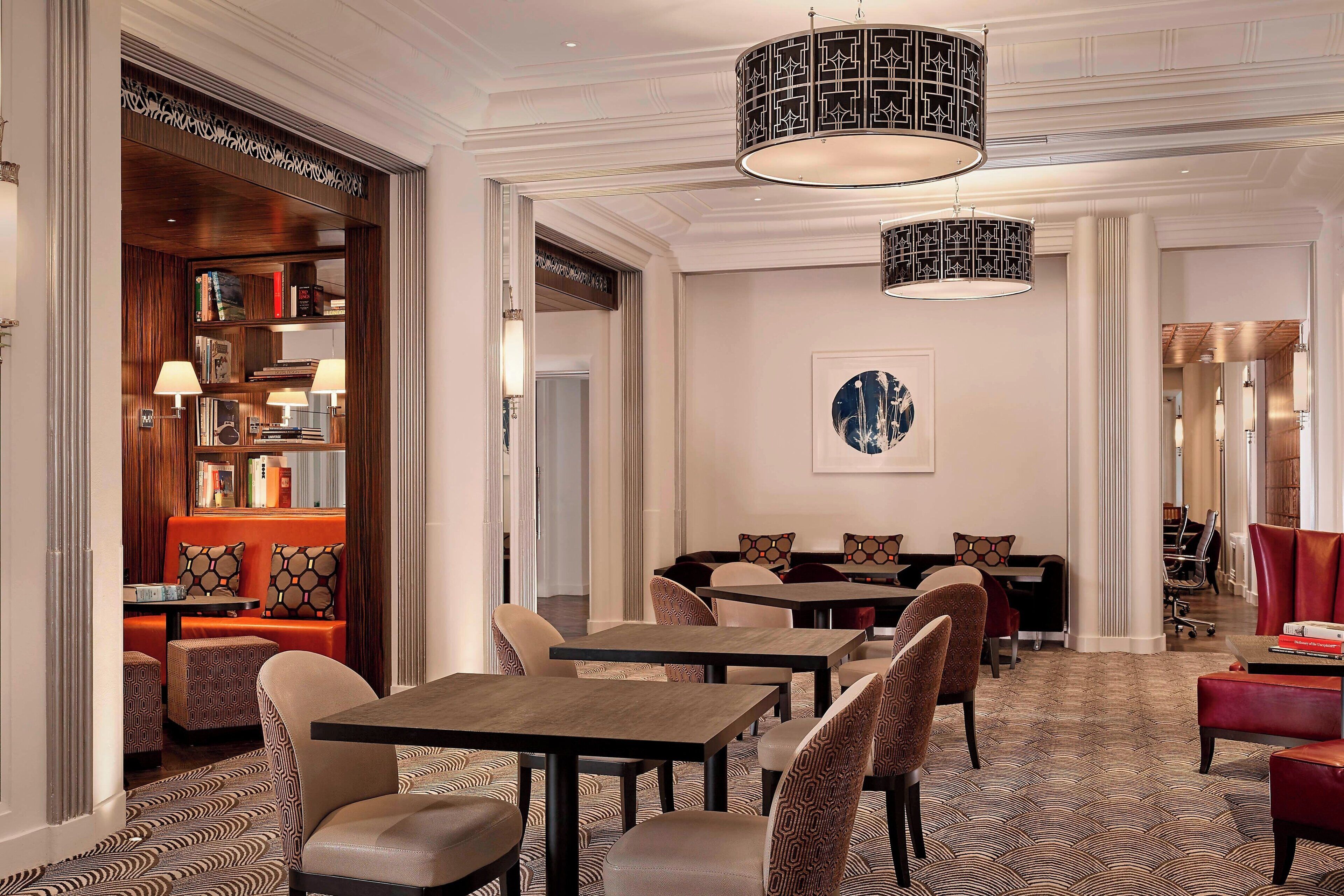 A hotel lobby with a patterned carpet, multiple seating areas including a sofa and tables, and a large abstract painting on the wall.