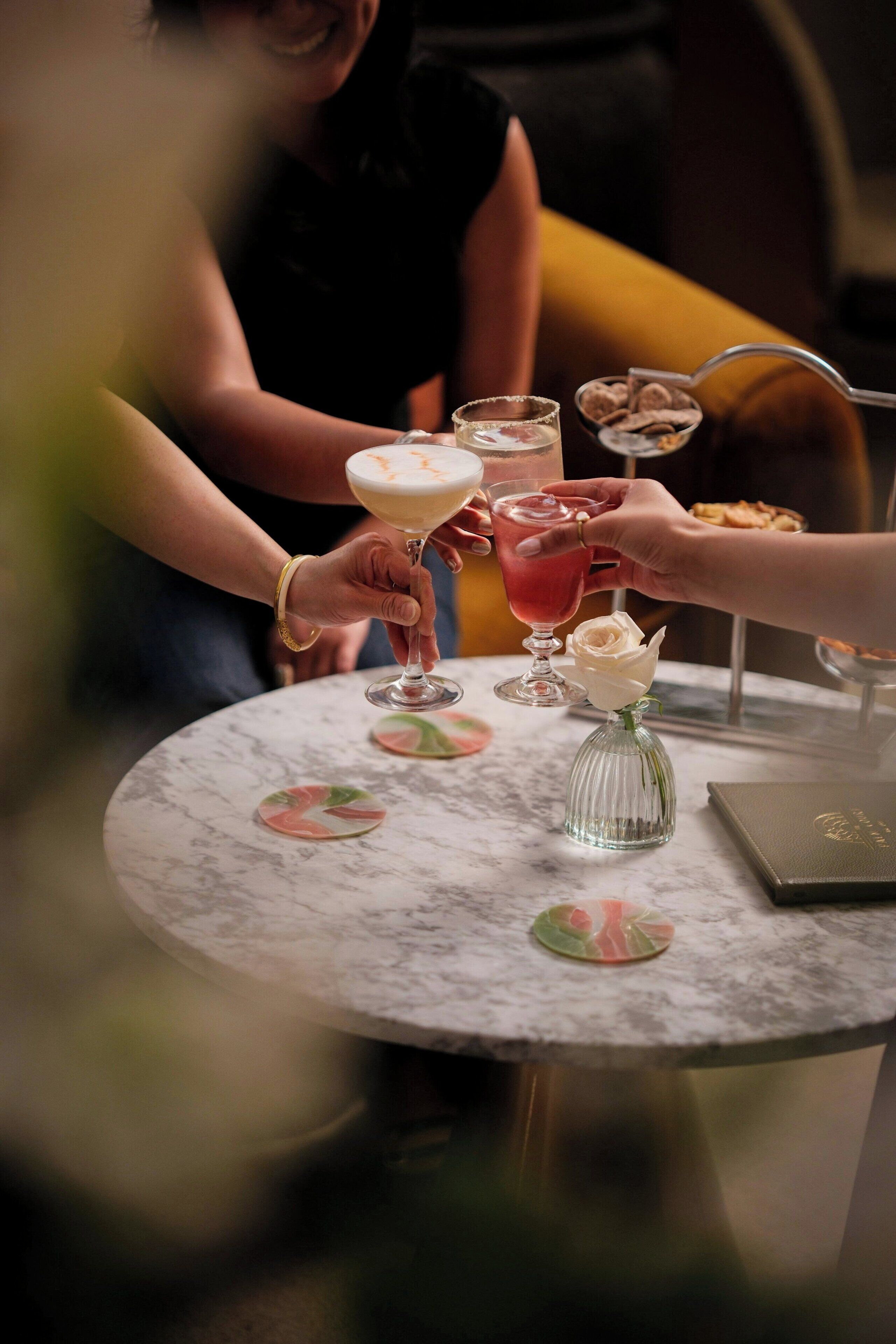 A round marble table with a glass of red drink, a white rose in a glass vase, and a laptop.