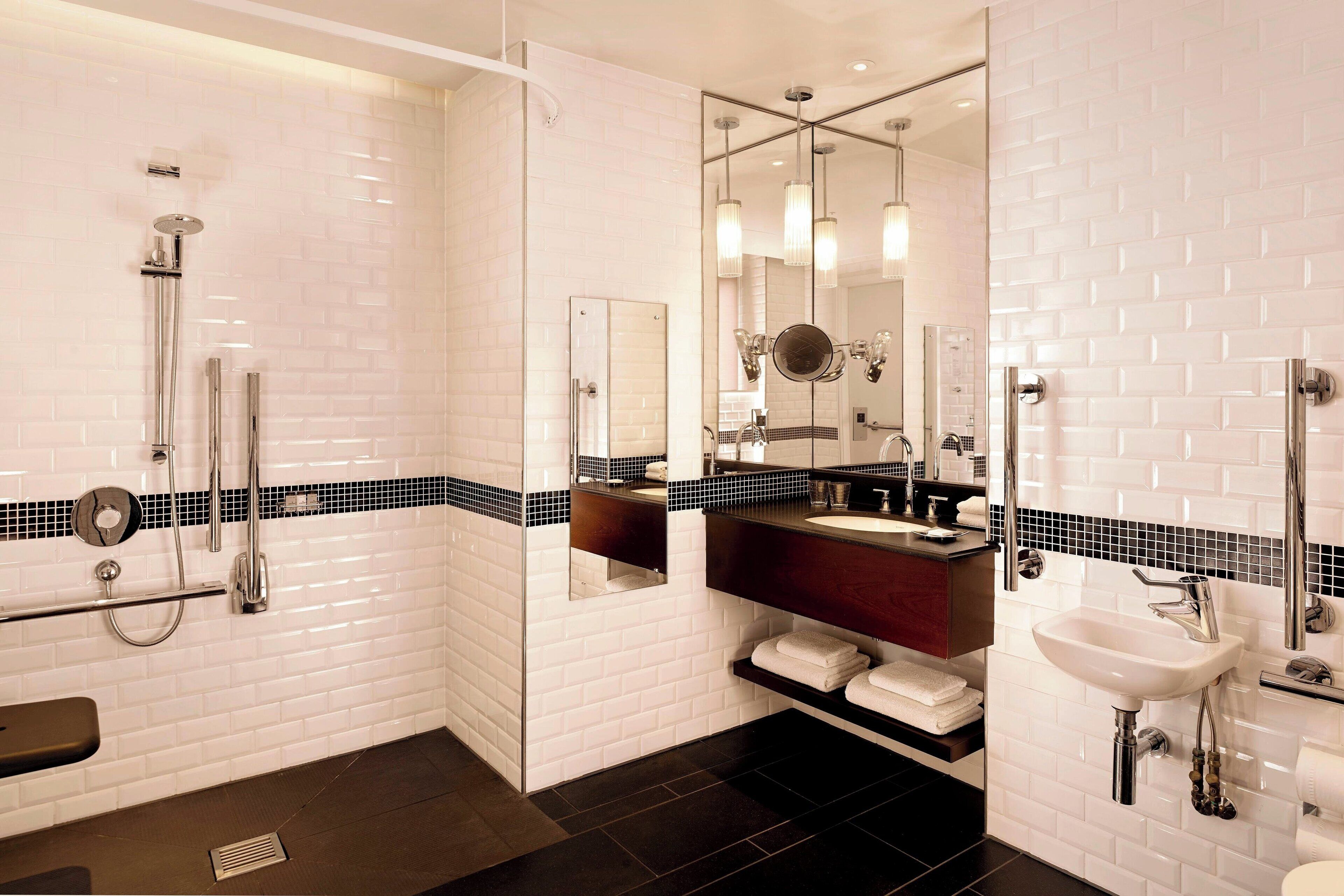 A modern bathroom with white subway tiles, a black and white tiled shower area, a vanity with a mirror, and a sink.
