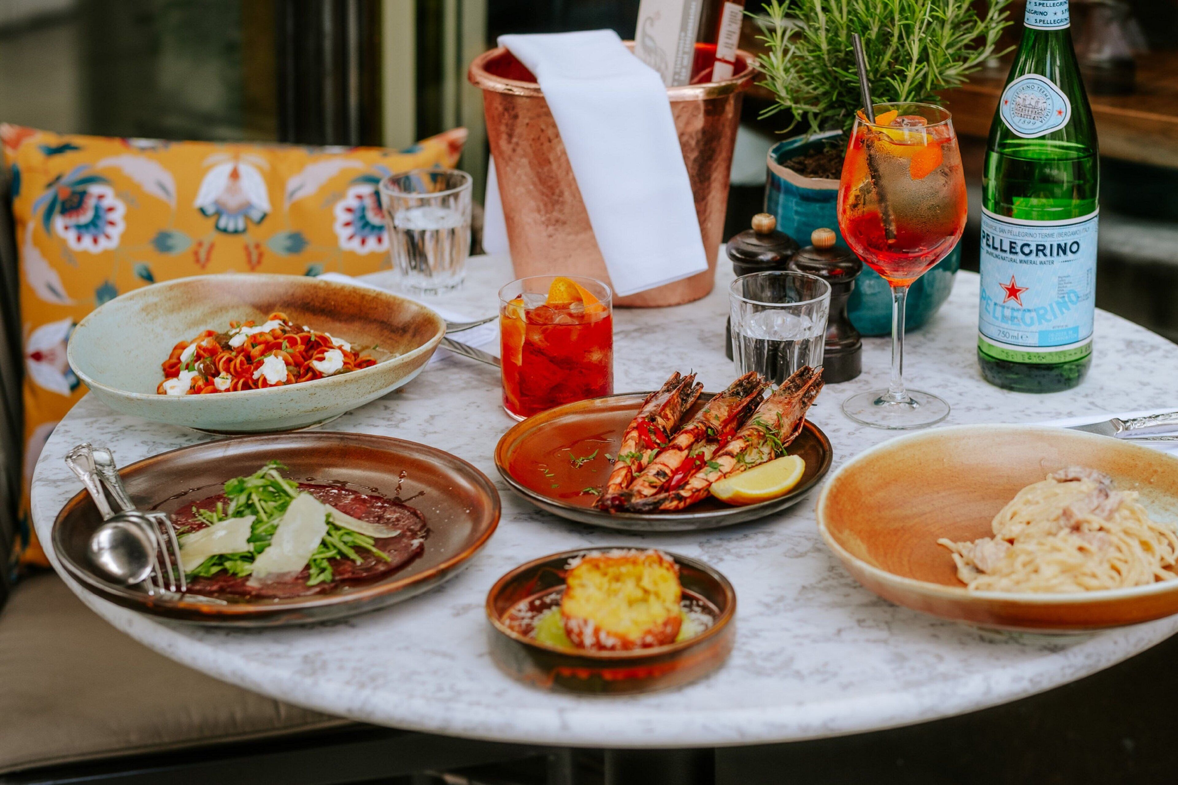 A table set with various dishes, drinks, and a bottle of Pellegrino water.