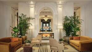 A spacious living room with a fireplace, two sofas, a coffee table, and large potted plants. - Sheraton Grand London Park Lane (London)