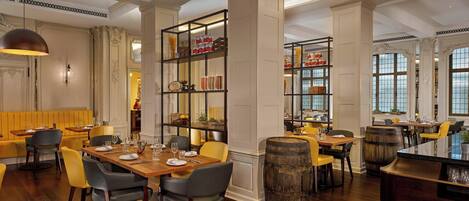 A spacious dining area with wooden tables and chairs, a central bar area with a barrel, and a large bookshelf filled with books and decorative items.