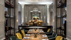 A dining area with a long wooden table set for a meal, surrounded by chairs with yellow and green upholstery. - Sheraton Grand London Park Lane (London)