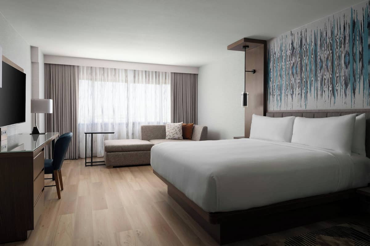 Una habitación de hotel con una cama grande, un escritorio, una silla, un sofá y un televisor.