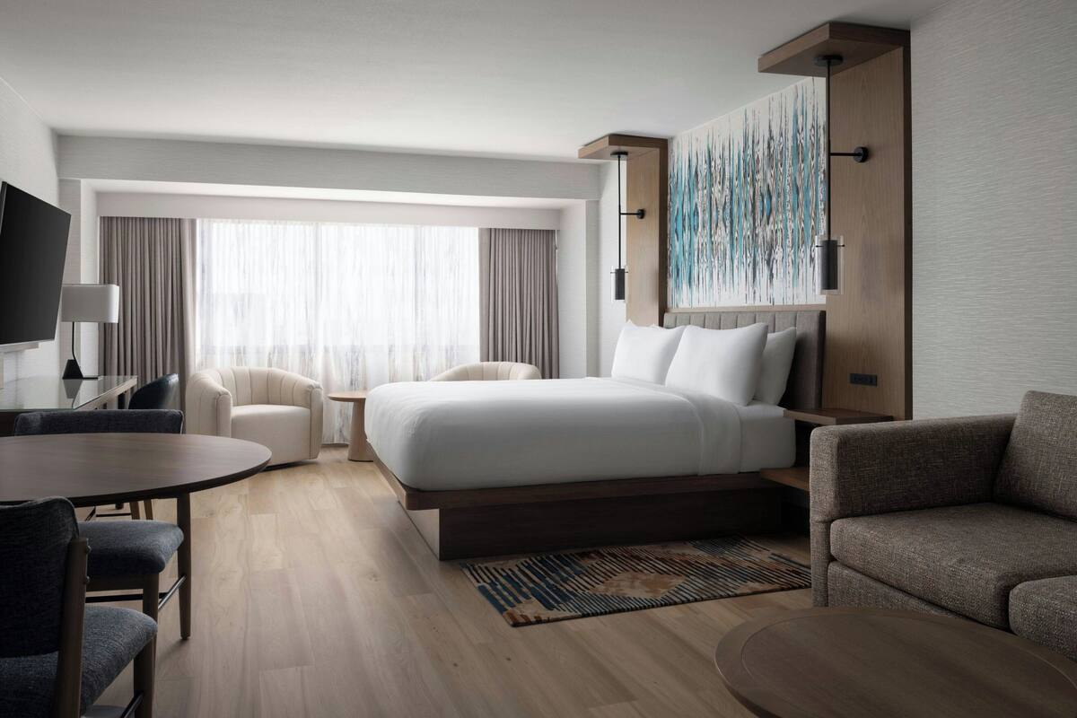 Una habitación de hotel moderna con una cama grande, un escritorio, un sofá y un televisor.