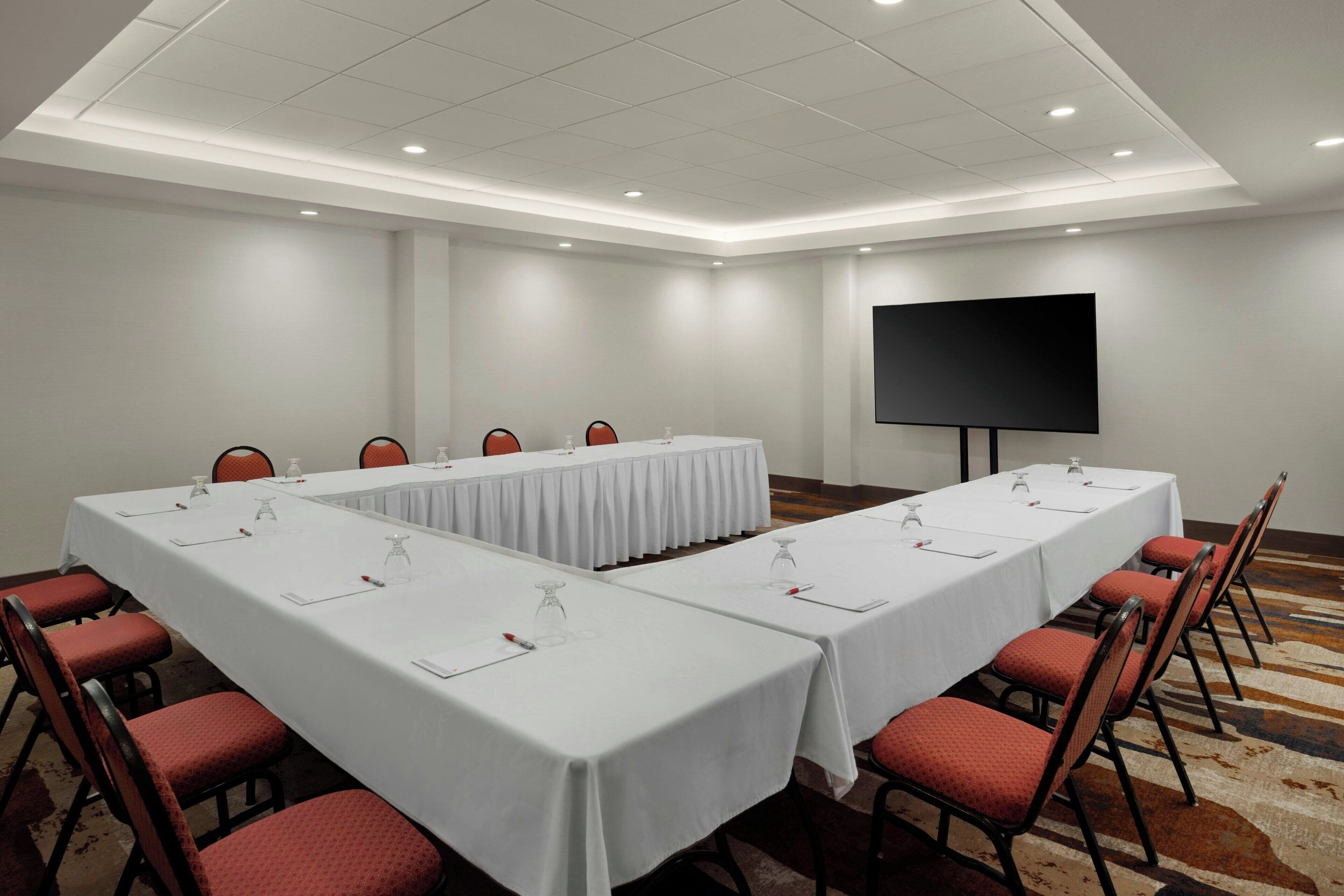 Un salón de conferencias con una larga mesa, sillas rojas y una pantalla grande.