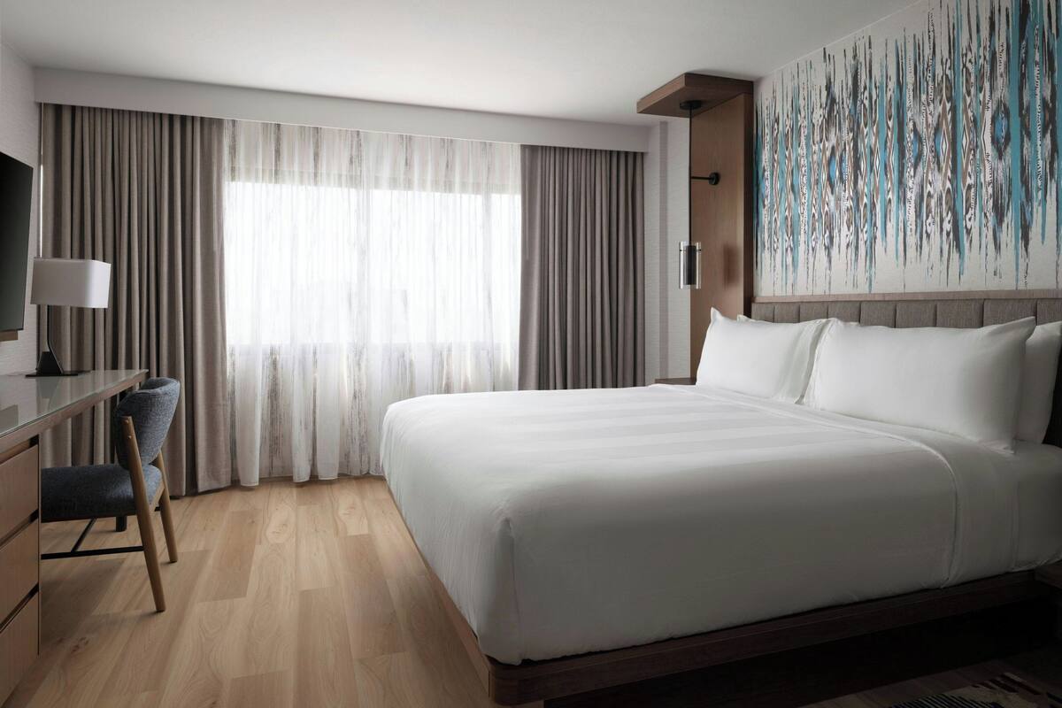 Una habitación de hotel moderna con una cama grande, un escritorio con una silla y un televisor.