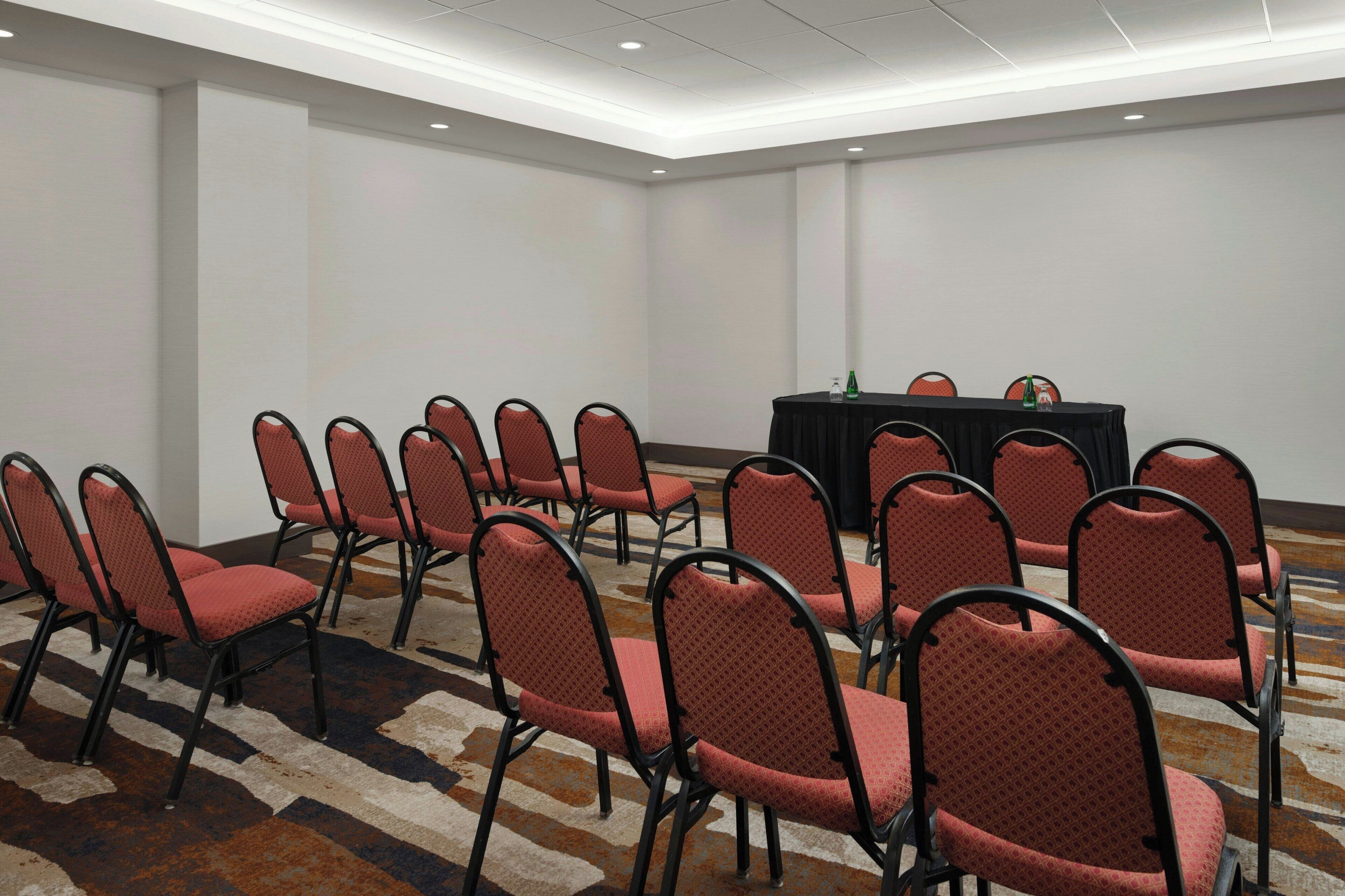 A conference room with rows of red chairs and a black table with a green bottle.