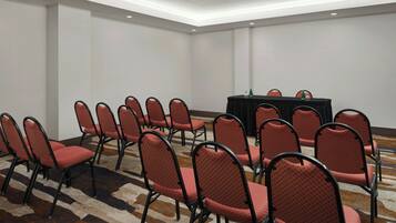A conference room with rows of red chairs and a black table with a green bottle.