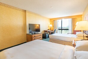 A hotel room with two beds, a television, a desk with a chair, and a window with curtains.