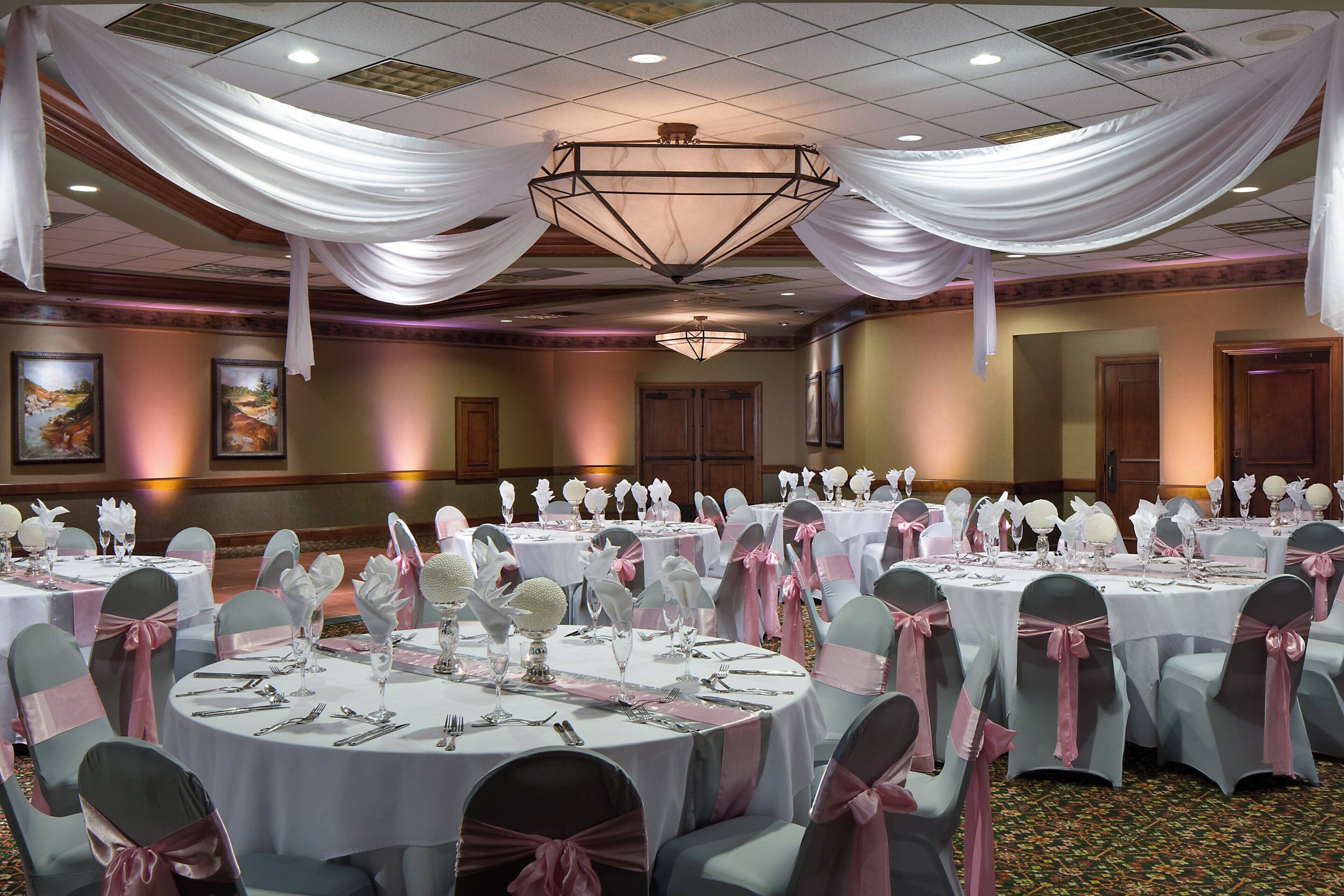 A banquet hall with round tables, white tablecloths, and chairs with pink sashes.