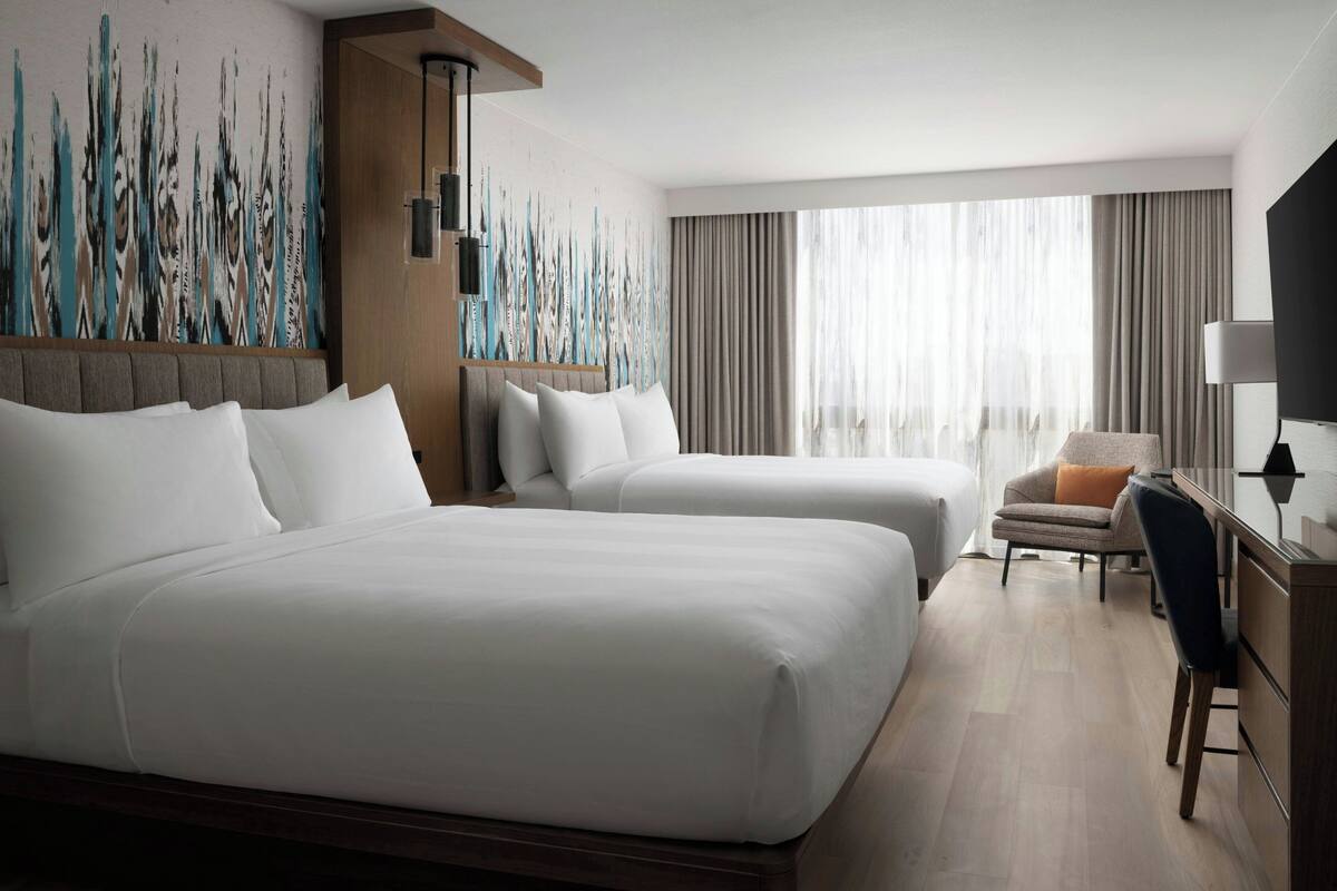 Habitación de hotel con dos camas, un escritorio, una silla y un cuadro abstracto grande en la pared.