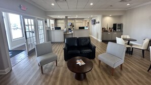 Un hall d’hôtel avec un comptoir de réception, un espace salon avec des chaises et un canapé, une petite table basse et, au fond, un coin cuisine.