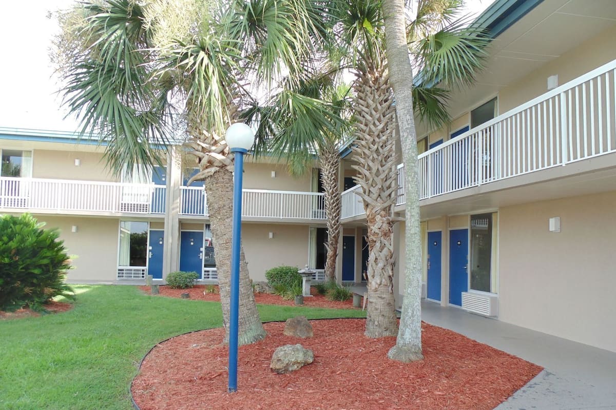 A multi-story hotel with balconies, palm trees, and a well-maintained lawn.