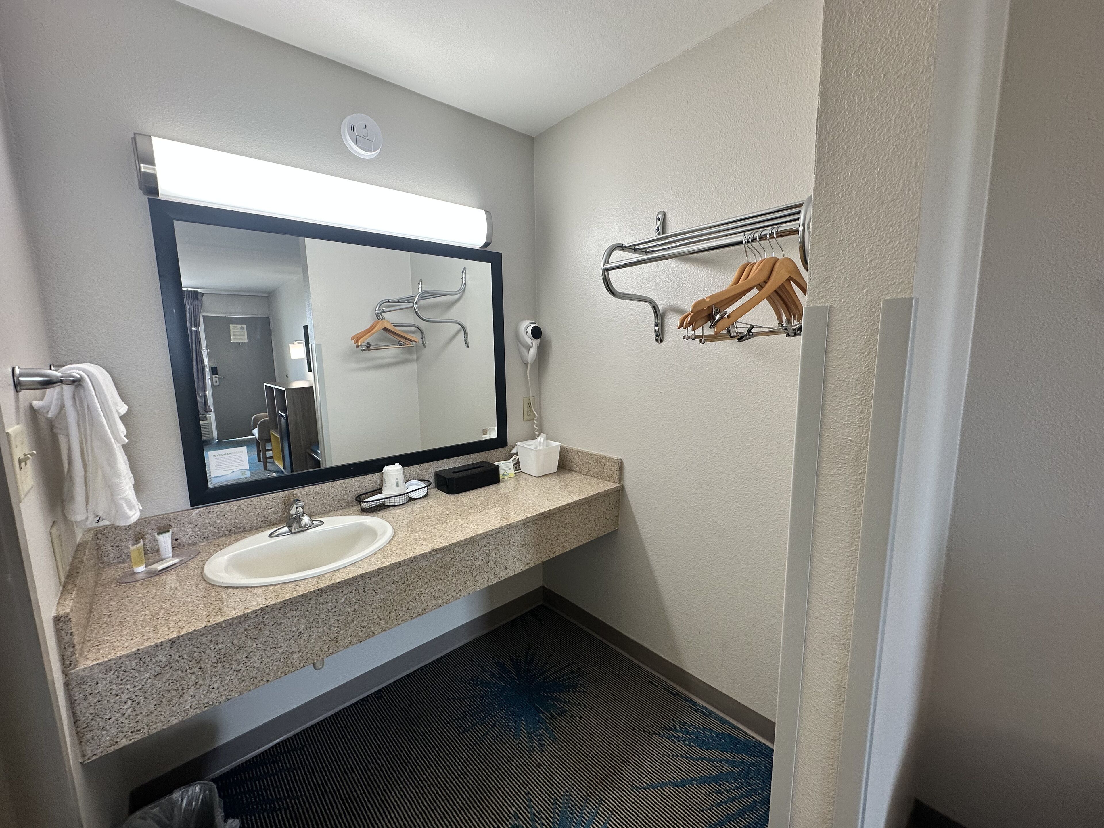 A compact hotel bathroom with a sink, mirror, towel rack, and a hairdryer.