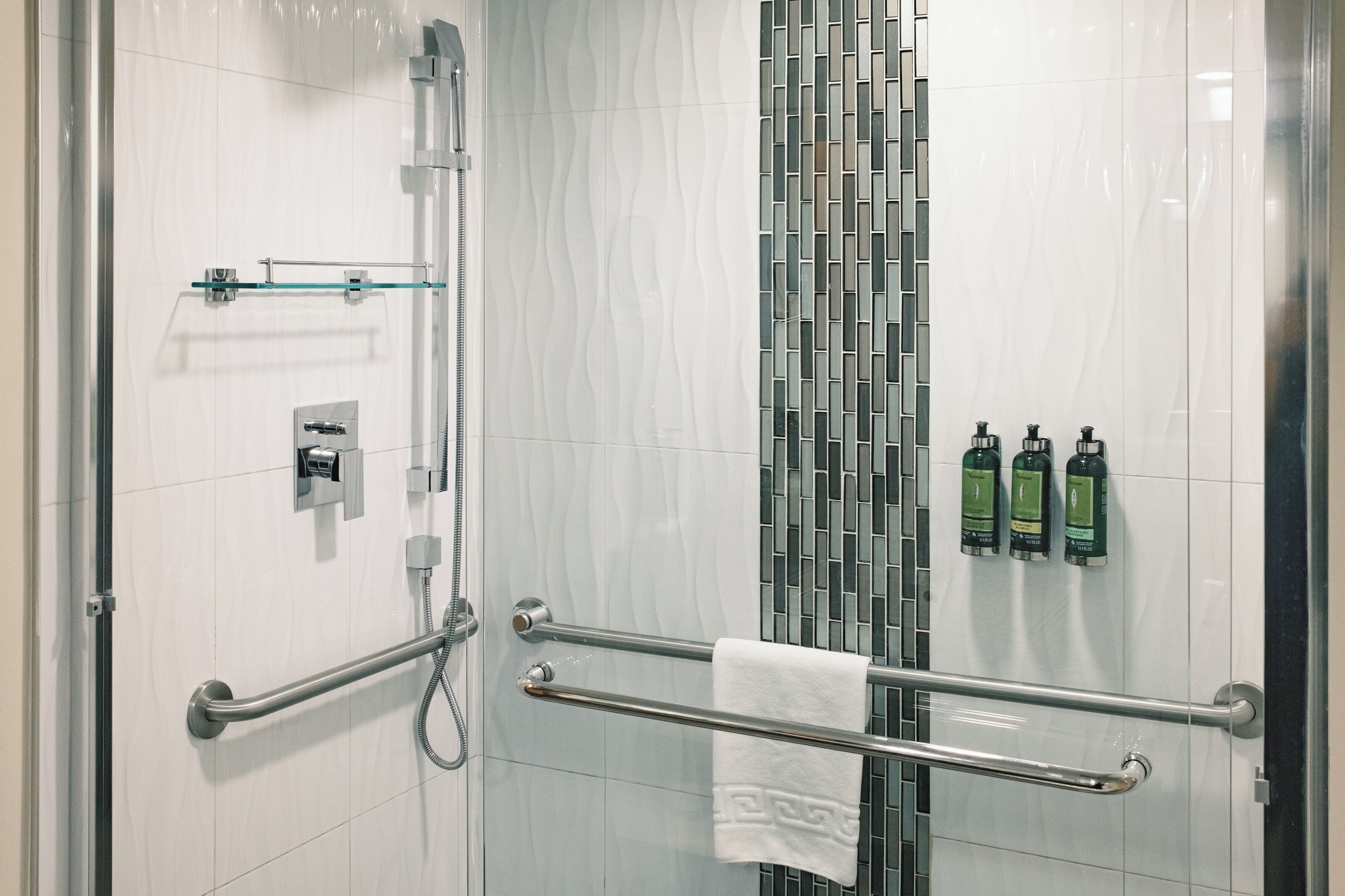 A shower area with a glass door, a towel rack, and three bottles of shampoo on the wall.