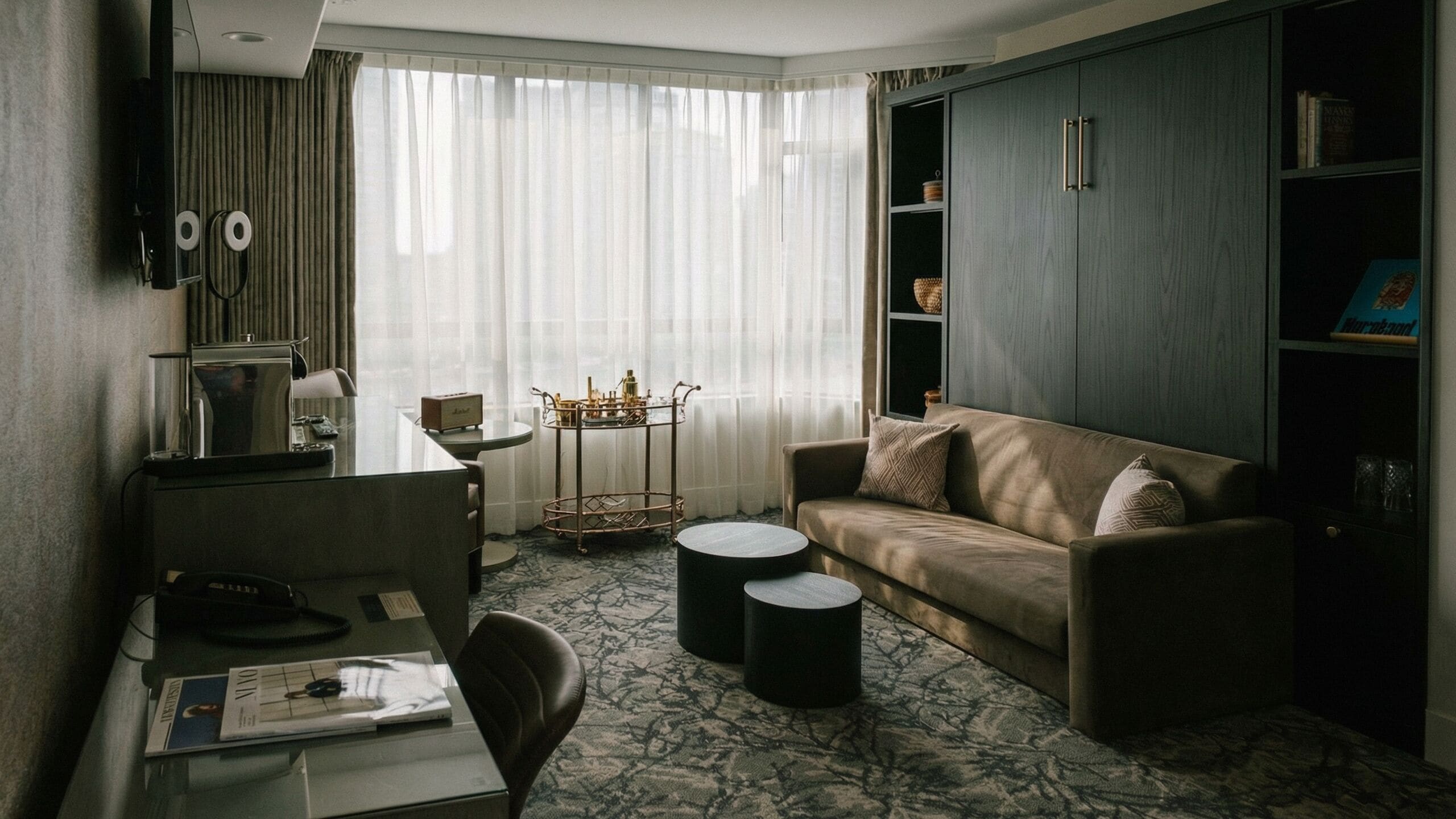 Una habitación de hotel con un sofá, un escritorio con una computadora portátil, una mesa de centro y una estantería.