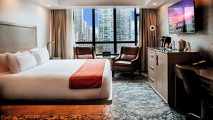 Habitación de hotel con una cama grande, dos sillones, un escritorio y un televisor montado en la pared.