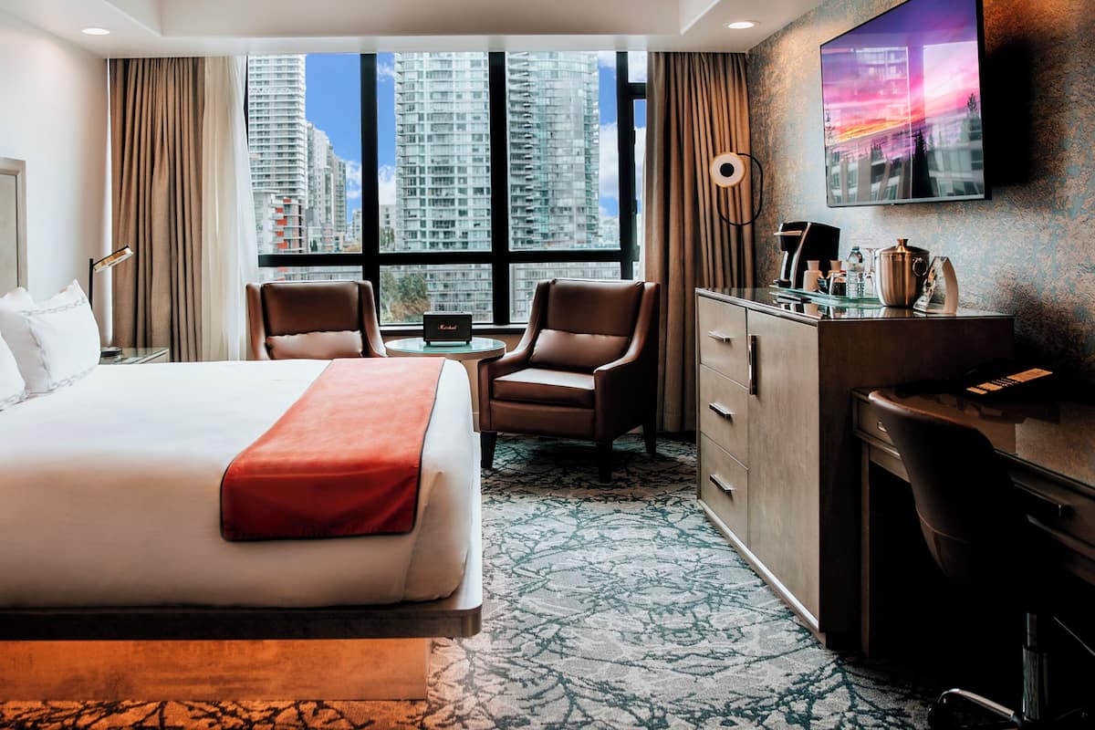 A hotel room with a large bed, two armchairs, a desk, and a TV mounted on the wall.