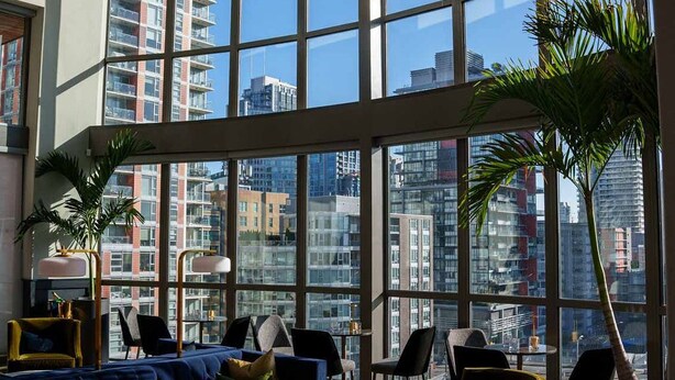 Un salón amplio con ventanas grandes, un sofá azul, sillas amarillas y una planta en maceta.