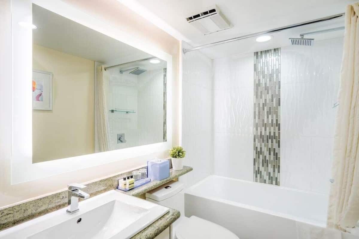A bathroom with a large mirror, a sink, a toilet, and a shower with a curtain.