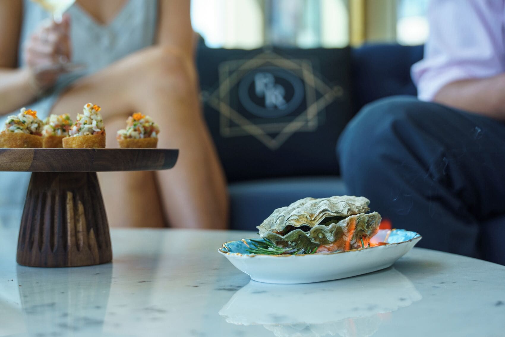 A table with a dish of oysters on the half shell and a wooden stand with small appetizers.