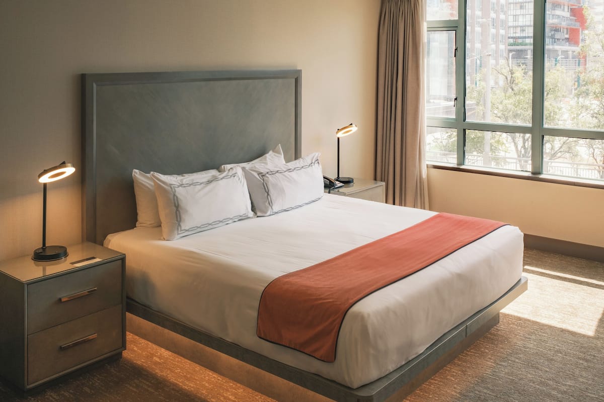 A neatly made bed with a grey headboard, two bedside tables with lamps, and a window with curtains.