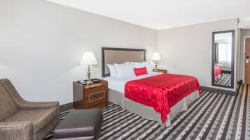 A hotel room with a bed, a chair, a nightstand, and a mirror.