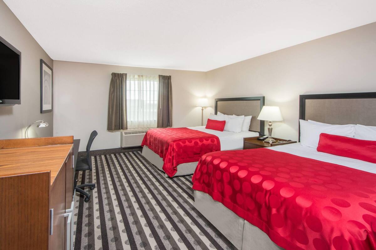 A hotel room with two beds, a desk, a chair, a TV, and a window with curtains.