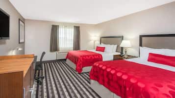 A hotel room with two beds, a desk, a chair, a TV, and a window with curtains.