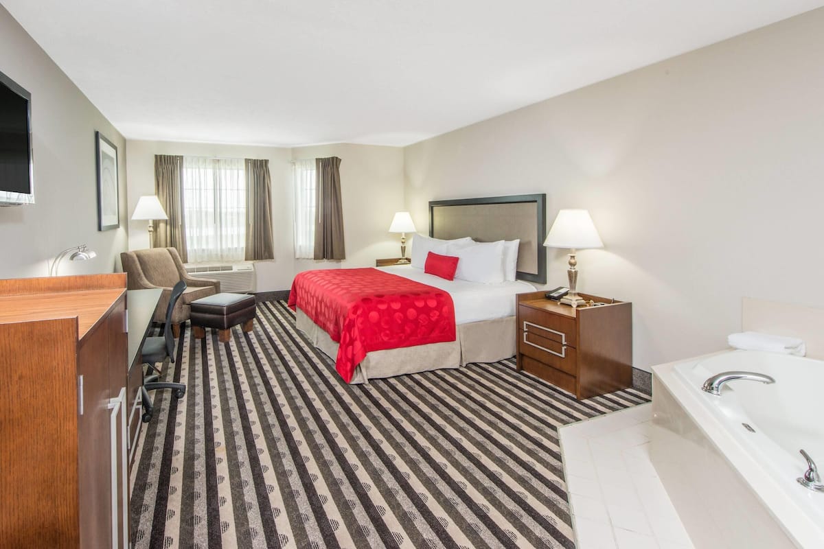 A hotel room with a bed, desk, chair, and a large bathroom with a bathtub.