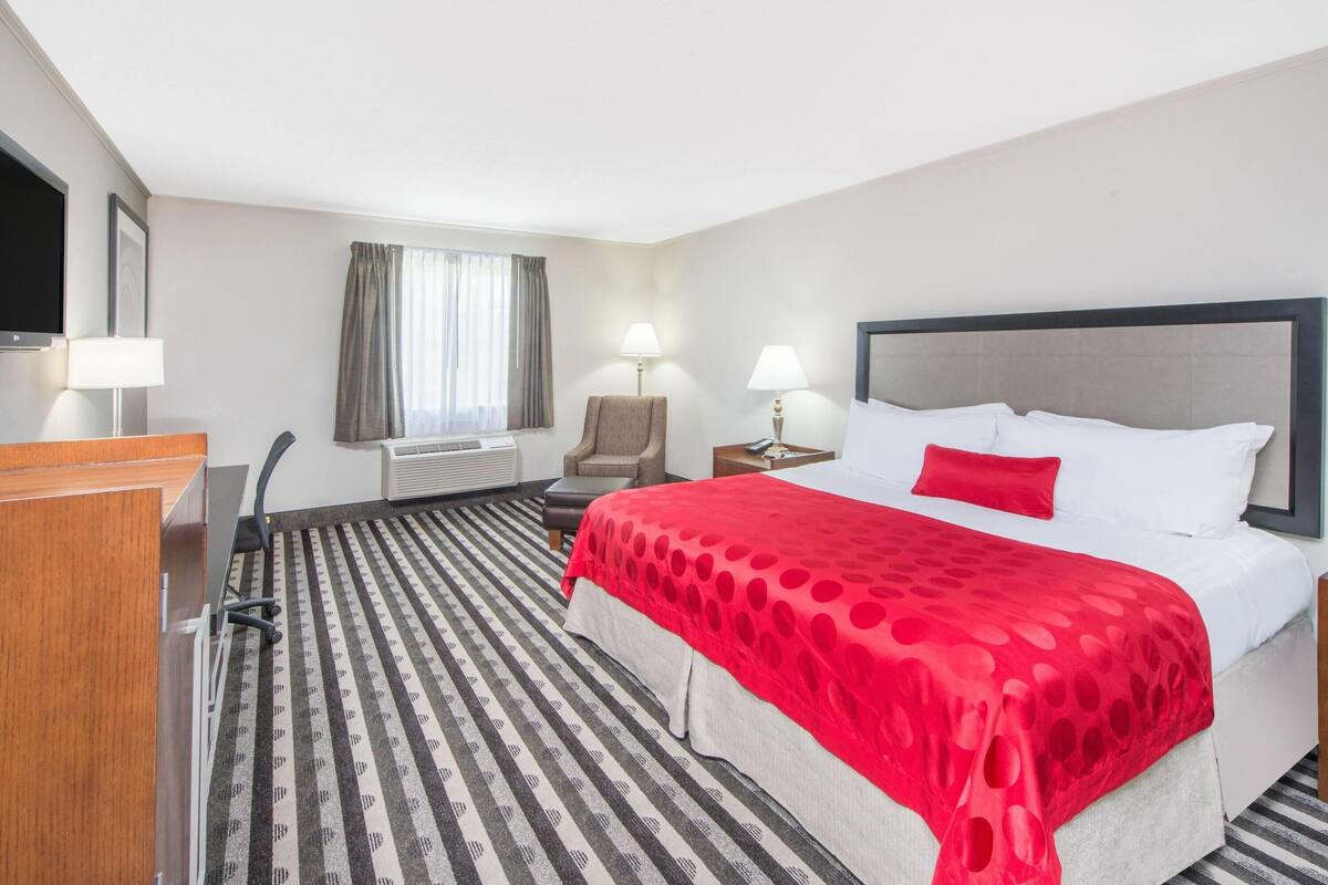 A hotel room with a bed, a desk, a chair, two bedside lamps, and a window with curtains.
