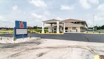A motel with a large sign, a covered parking area, and a building with a sloped roof.