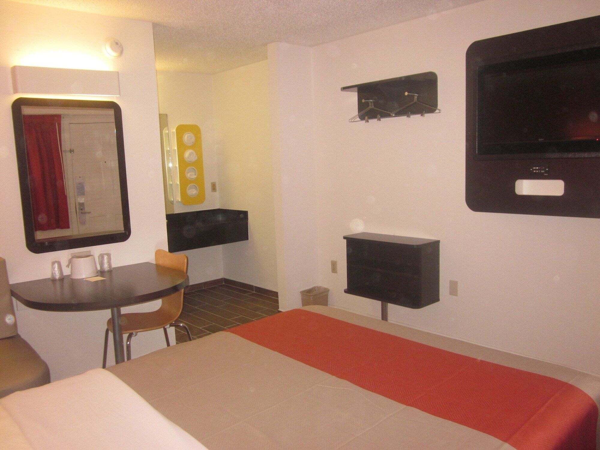 Una habitación de hotel con cama, una mesita con sillas, televisión y estante en la pared.