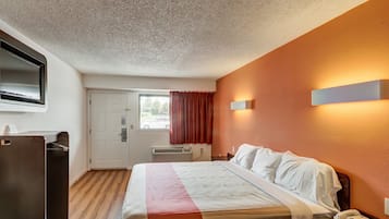 Et hotelværelse med seng, skrivebord, telefon, fjernsyn og et vindue med gardiner.