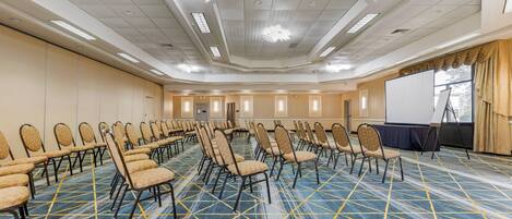 A conference room with rows of chairs, a projector screen, and a carpeted floor.