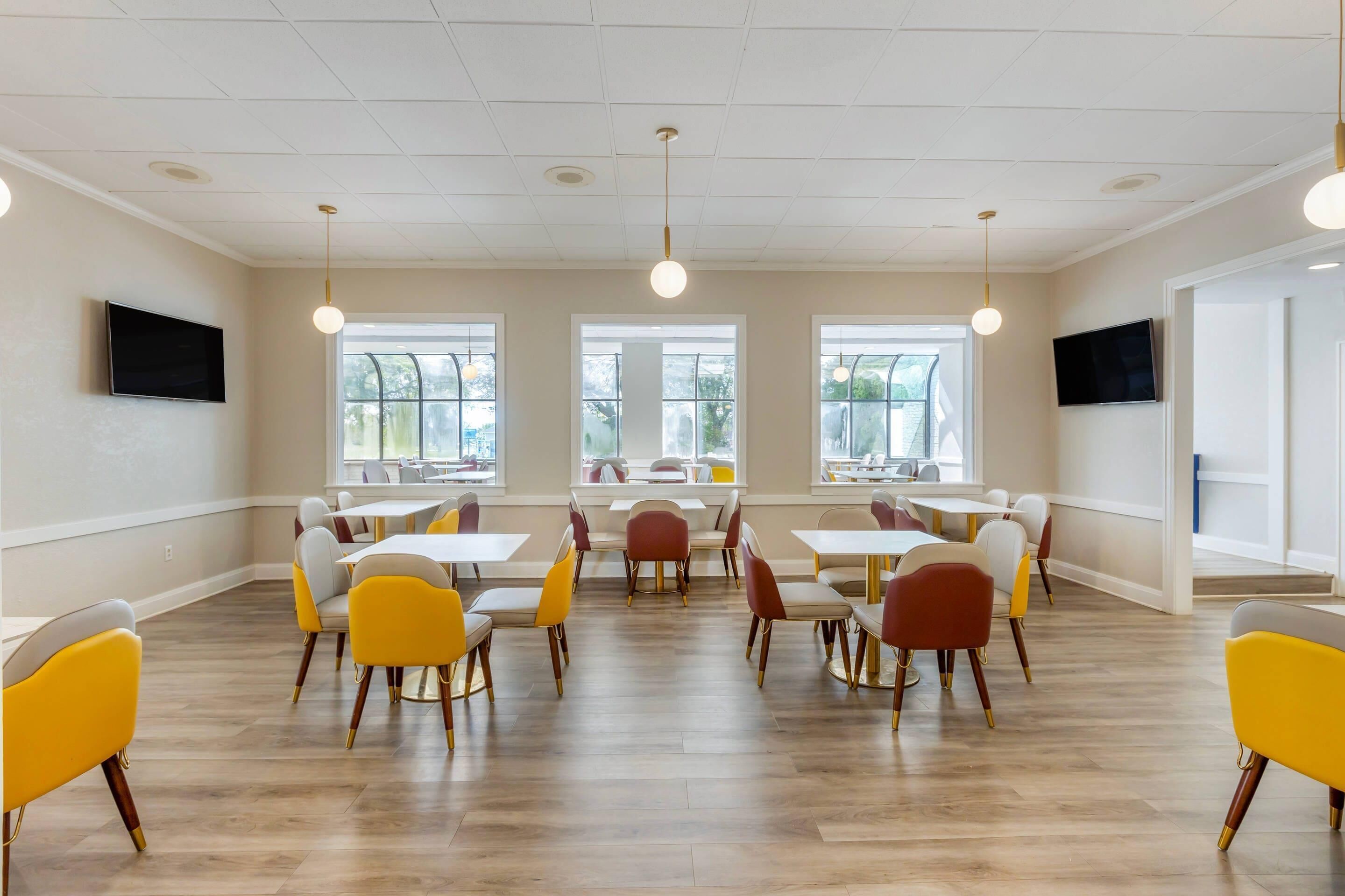 Et moderne spiseområde med flere borde og stole, store vinduer og loftslamper.