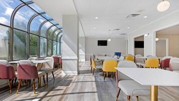 A modern dining area with large windows, white tables, and colorful chairs.