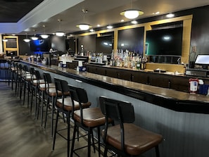 Un espace bar doté d’un long comptoir, de nombreux tabourets et d’une grande variété de bouteilles et de verres.
