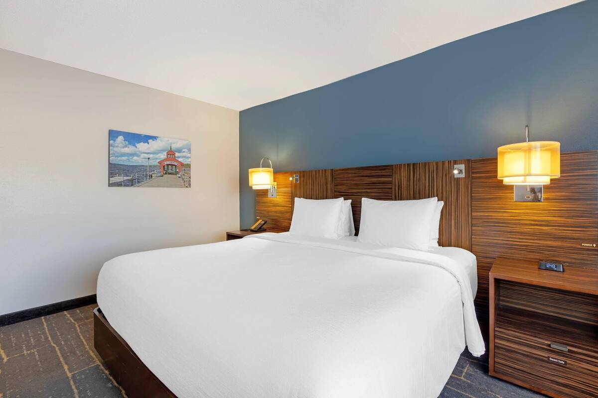A hotel room with a large bed, wooden headboard, two bedside lamps, a nightstand, and a wall-mounted TV.
