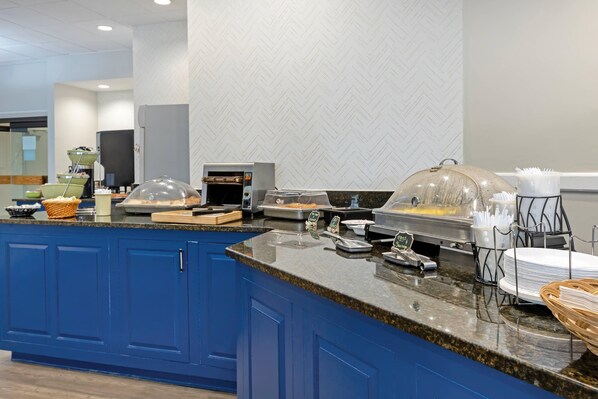 A kitchen with blue cabinets, a granite countertop, and a buffet setup with food items and utensils.