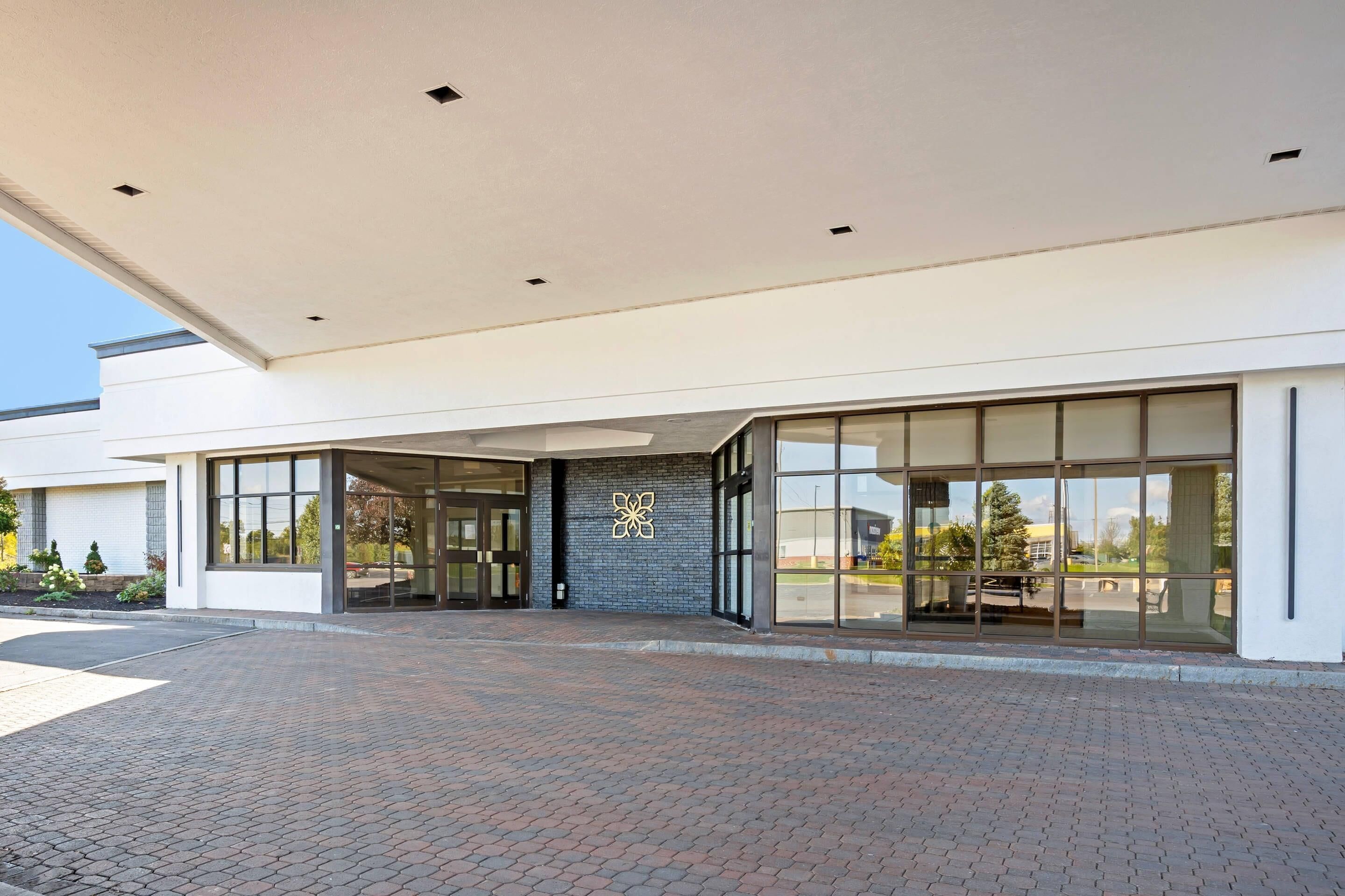 A modern building with a brick-paved entrance, large glass doors, and a geometric wall design.
